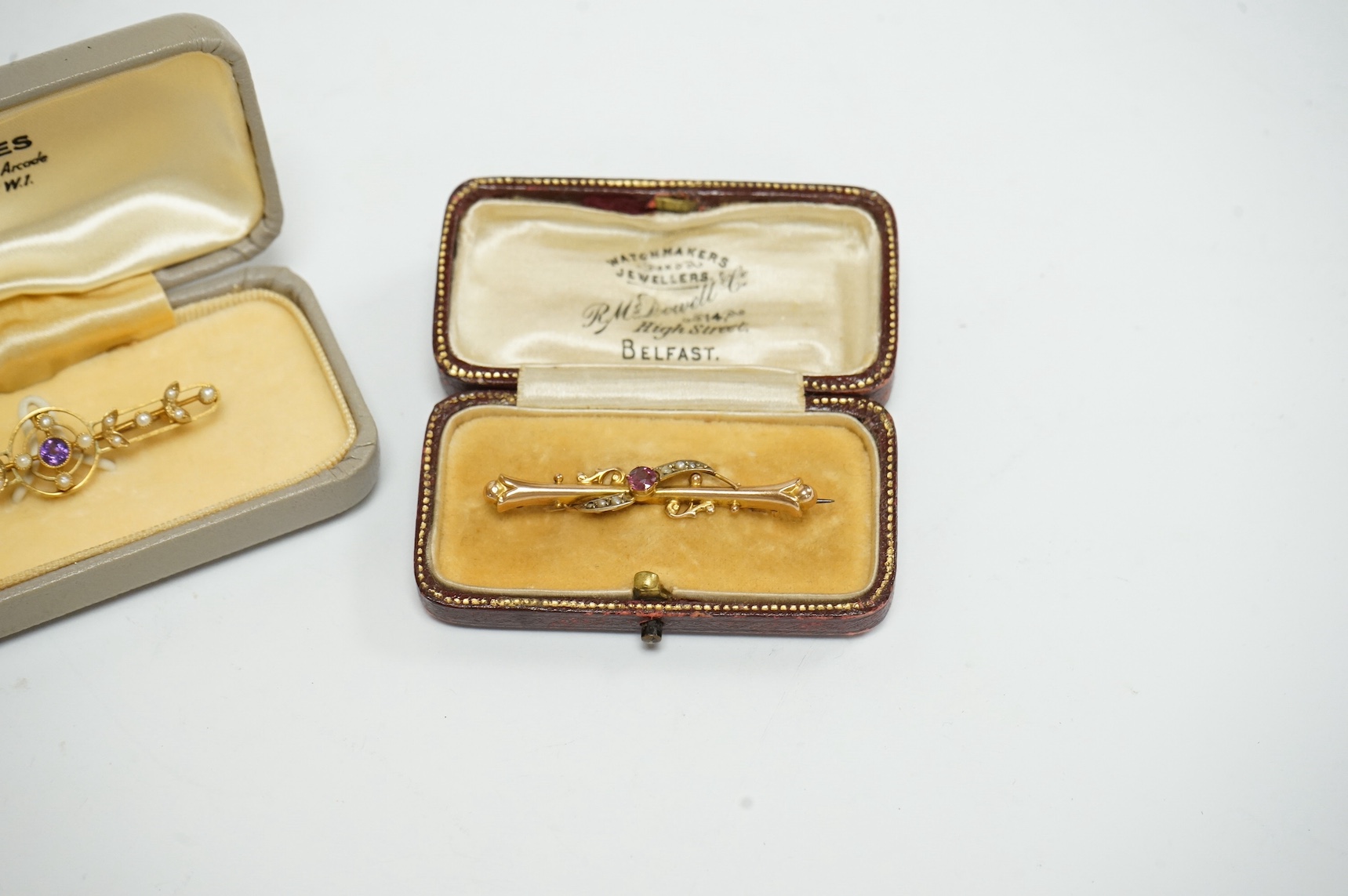 Two bar brooches, early 20th century, comprising: one set with a circular-cut garnet, accented by seed pearls, mounted in 9ct gold, length 4.4cm, British hallmarks; and another set with a circular-cut amethyst and seed p